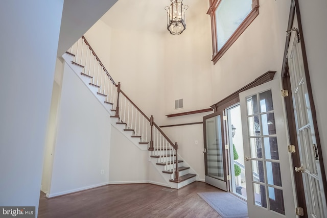 entrance foyer with french doors, a towering ceiling, hardwood / wood-style floors, and a notable chandelier