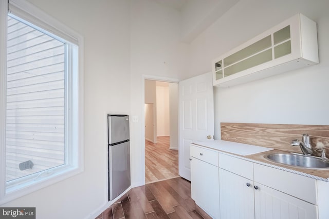 kitchen with sink, stainless steel refrigerator, white cabinetry, a healthy amount of sunlight, and dark hardwood / wood-style flooring