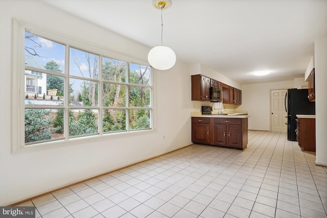 kitchen with decorative light fixtures, dark brown cabinetry, black refrigerator, and plenty of natural light