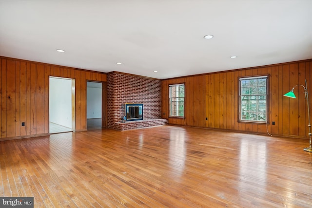 unfurnished living room featuring wooden walls, a fireplace, light hardwood / wood-style floors, and crown molding