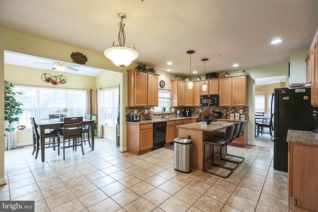 kitchen with decorative light fixtures, light tile patterned flooring, light stone countertops, black appliances, and a center island