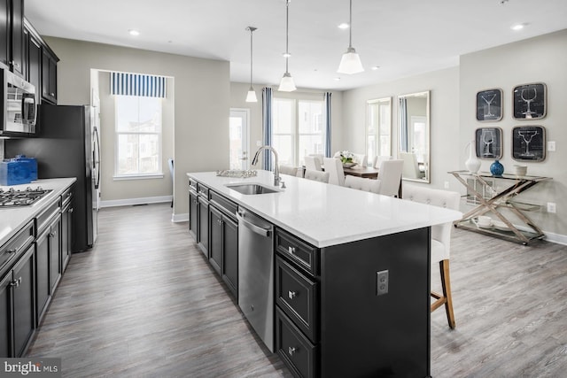 kitchen featuring decorative light fixtures, an island with sink, appliances with stainless steel finishes, a kitchen breakfast bar, and sink