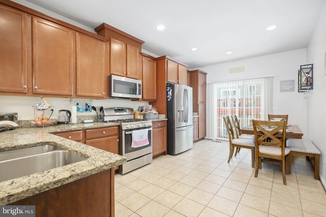 kitchen featuring stainless steel appliances, sink, light tile patterned floors, and light stone counters