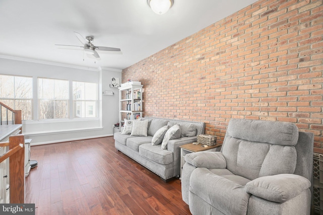 living room featuring ceiling fan, dark wood-type flooring, crown molding, and brick wall