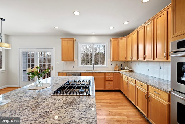 kitchen featuring pendant lighting, sink, stainless steel appliances, light stone counters, and light wood-type flooring