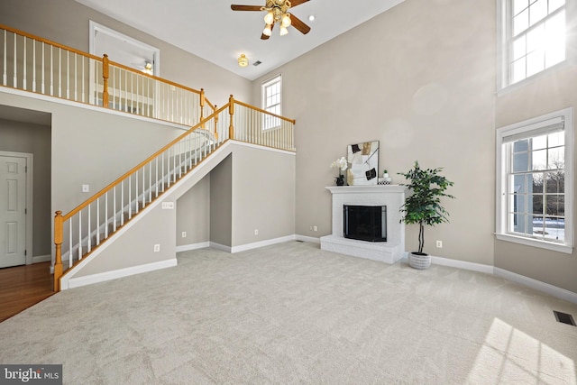 unfurnished living room featuring carpet flooring, a fireplace, a wealth of natural light, and a high ceiling