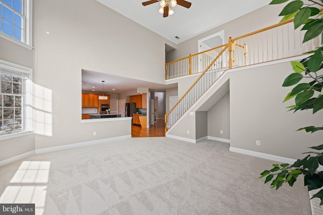 unfurnished living room featuring light colored carpet, ceiling fan, and a high ceiling