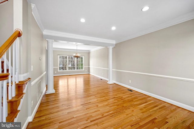 empty room featuring ornamental molding, a chandelier, light wood-type flooring, and ornate columns