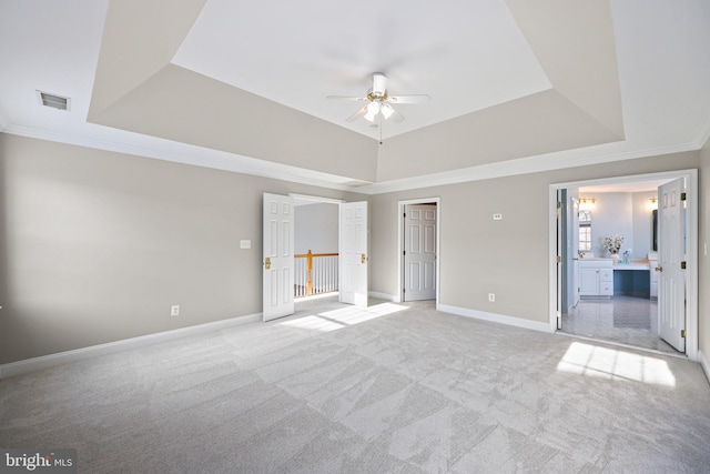 unfurnished bedroom featuring a raised ceiling, ceiling fan, light colored carpet, and ensuite bath