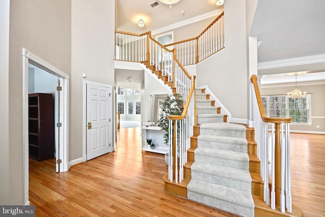 staircase with a towering ceiling, ornamental molding, a chandelier, and wood-type flooring