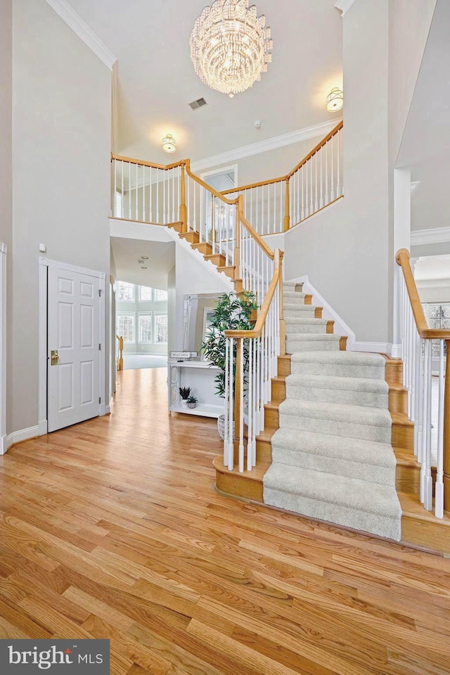 staircase featuring hardwood / wood-style flooring, ornamental molding, and an inviting chandelier