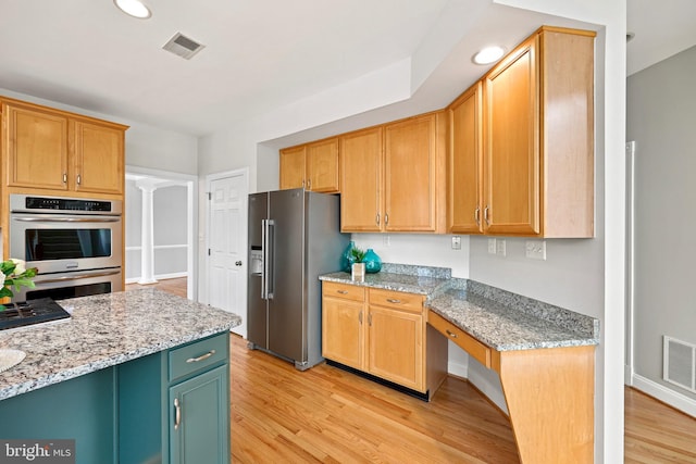 kitchen featuring light stone counters, appliances with stainless steel finishes, built in desk, and light wood-type flooring