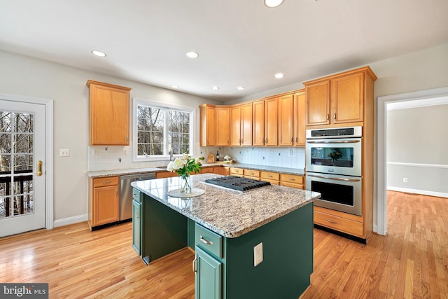 kitchen featuring sink, light stone counters, appliances with stainless steel finishes, a kitchen island, and light hardwood / wood-style floors