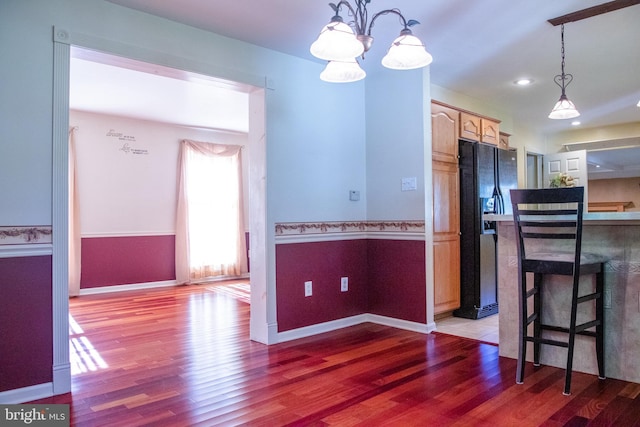 kitchen with an inviting chandelier, hardwood / wood-style flooring, pendant lighting, and black fridge