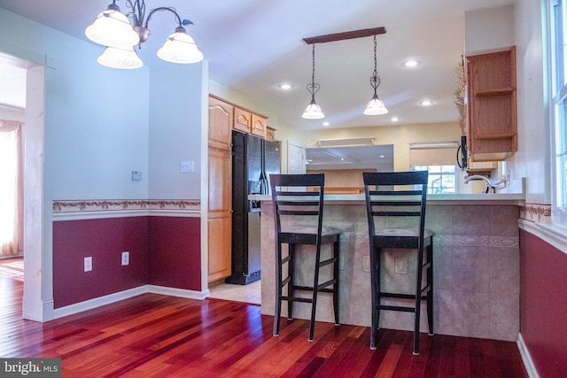 kitchen with dark wood-type flooring, black refrigerator with ice dispenser, a notable chandelier, and a kitchen breakfast bar