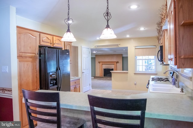 kitchen featuring black appliances, sink, hanging light fixtures, and a breakfast bar area