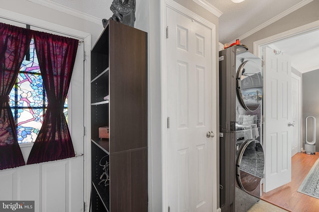 clothes washing area with a textured ceiling, ornamental molding, stacked washer and clothes dryer, and hardwood / wood-style floors