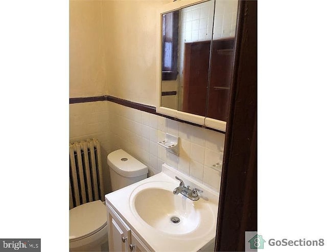 bathroom with tile walls, toilet, vanity, and radiator