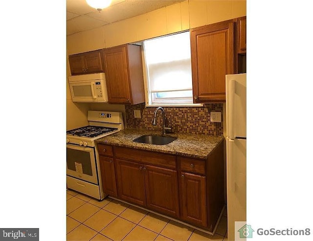 kitchen with white appliances, light tile patterned floors, decorative backsplash, dark stone countertops, and sink