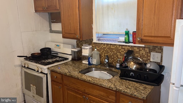 kitchen featuring white appliances, dark stone counters, backsplash, and sink