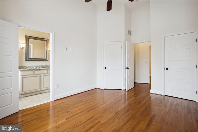 unfurnished bedroom with visible vents, baseboards, connected bathroom, a towering ceiling, and light wood-style flooring