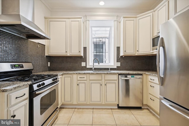 kitchen with stainless steel appliances, a sink, wall chimney range hood, cream cabinetry, and decorative backsplash