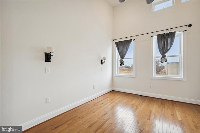 empty room featuring light wood-type flooring, a high ceiling, baseboards, and a ceiling fan