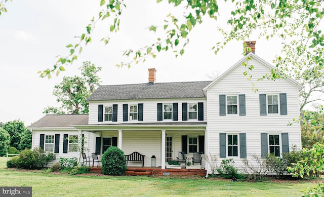 view of front of house featuring covered porch, a chimney, and a front lawn