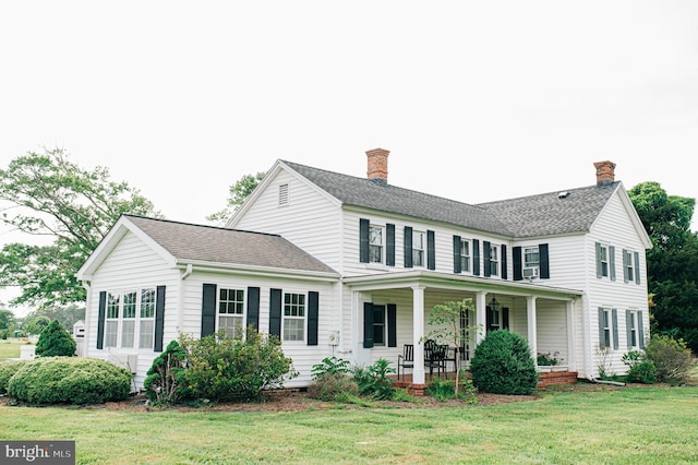 back of house featuring covered porch, a yard, a shingled roof, and a chimney