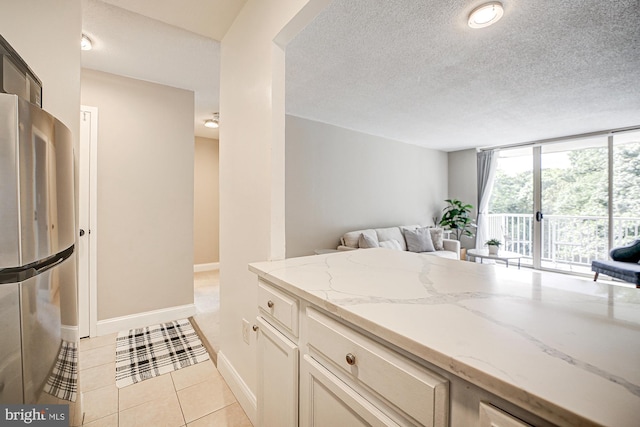 kitchen featuring light stone countertops, light tile patterned floors, stainless steel fridge, and a textured ceiling