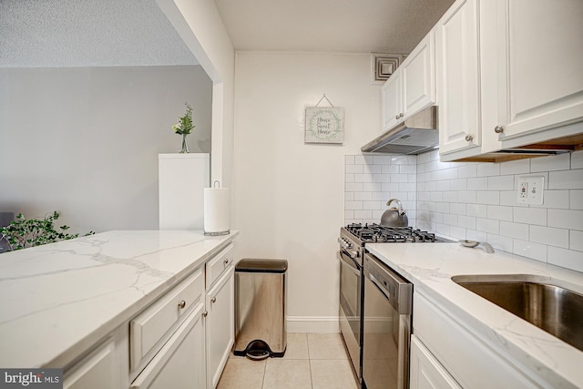 kitchen featuring light tile patterned floors, white cabinetry, light stone counters, stainless steel gas range oven, and a textured ceiling