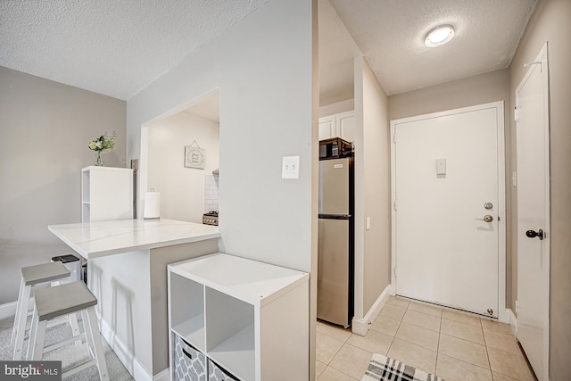 kitchen featuring light tile patterned flooring, a kitchen bar, stainless steel fridge, kitchen peninsula, and white cabinets