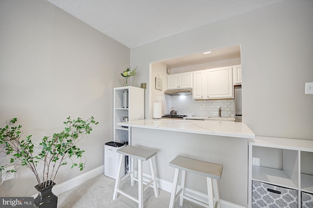 kitchen featuring white cabinetry, a kitchen breakfast bar, light stone counters, tasteful backsplash, and a textured ceiling