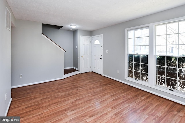 entryway with baseboards, a textured ceiling, visible vents, and wood finished floors