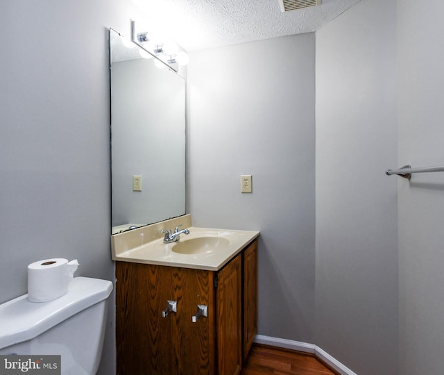 bathroom with a textured ceiling, toilet, wood finished floors, vanity, and baseboards