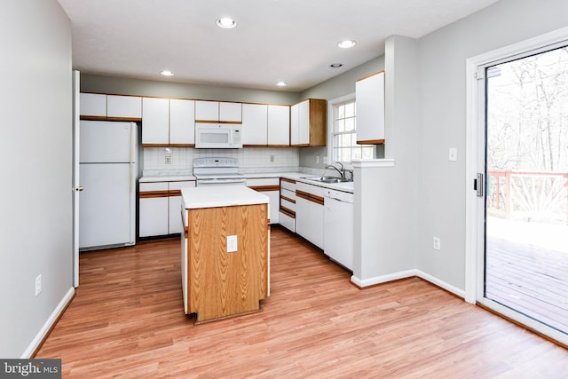 kitchen with white appliances, white cabinets, a center island, light countertops, and a sink