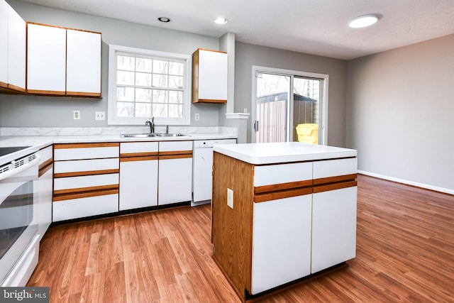 kitchen with white appliances, a sink, white cabinetry, light countertops, and light wood-type flooring