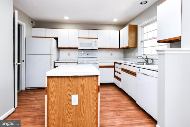 kitchen with white appliances, a sink, white cabinets, light countertops, and a center island