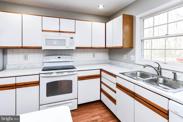 kitchen with light countertops, decorative backsplash, white cabinetry, a sink, and white appliances