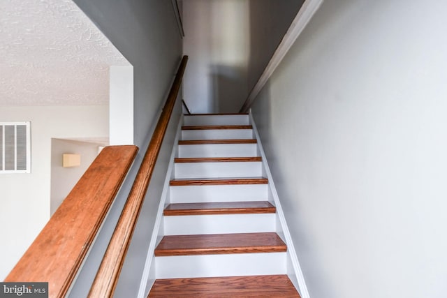 stairway featuring a textured ceiling, wood finished floors, visible vents, and baseboards