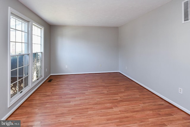 empty room with light wood-style floors, visible vents, baseboards, and a textured ceiling