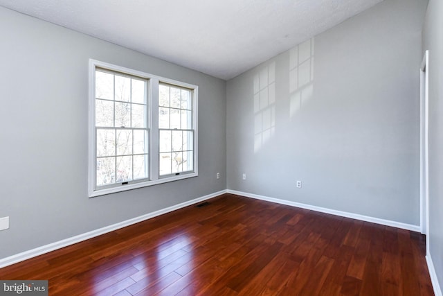 spare room featuring dark wood-type flooring, visible vents, and baseboards