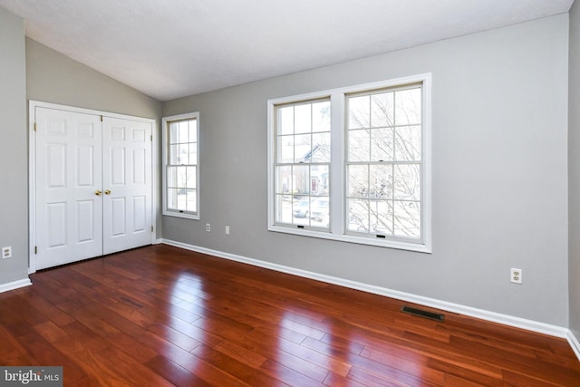 unfurnished bedroom featuring a closet, visible vents, dark wood-type flooring, vaulted ceiling, and baseboards