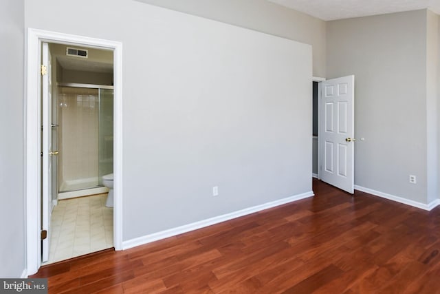 unfurnished bedroom featuring ensuite bath, baseboards, visible vents, and dark wood finished floors