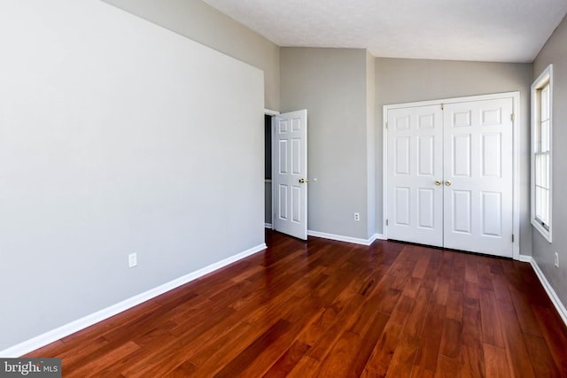 unfurnished bedroom with lofted ceiling, dark wood finished floors, and baseboards