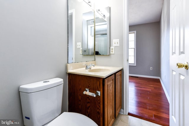 half bath with toilet, baseboards, and vanity