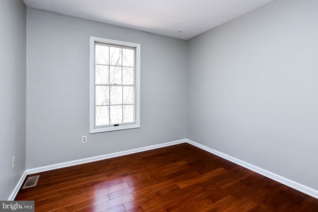 spare room with dark wood-type flooring, visible vents, and baseboards