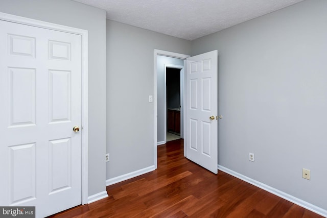 unfurnished bedroom featuring dark wood-style flooring, a textured ceiling, and baseboards