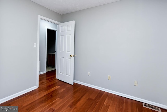 unfurnished room featuring a textured ceiling, dark wood finished floors, visible vents, and baseboards