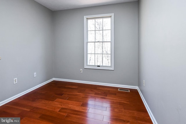 unfurnished room featuring dark wood-style floors, visible vents, and baseboards